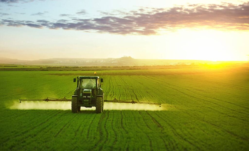 Tractor spraying a field of wheat with fertilizer